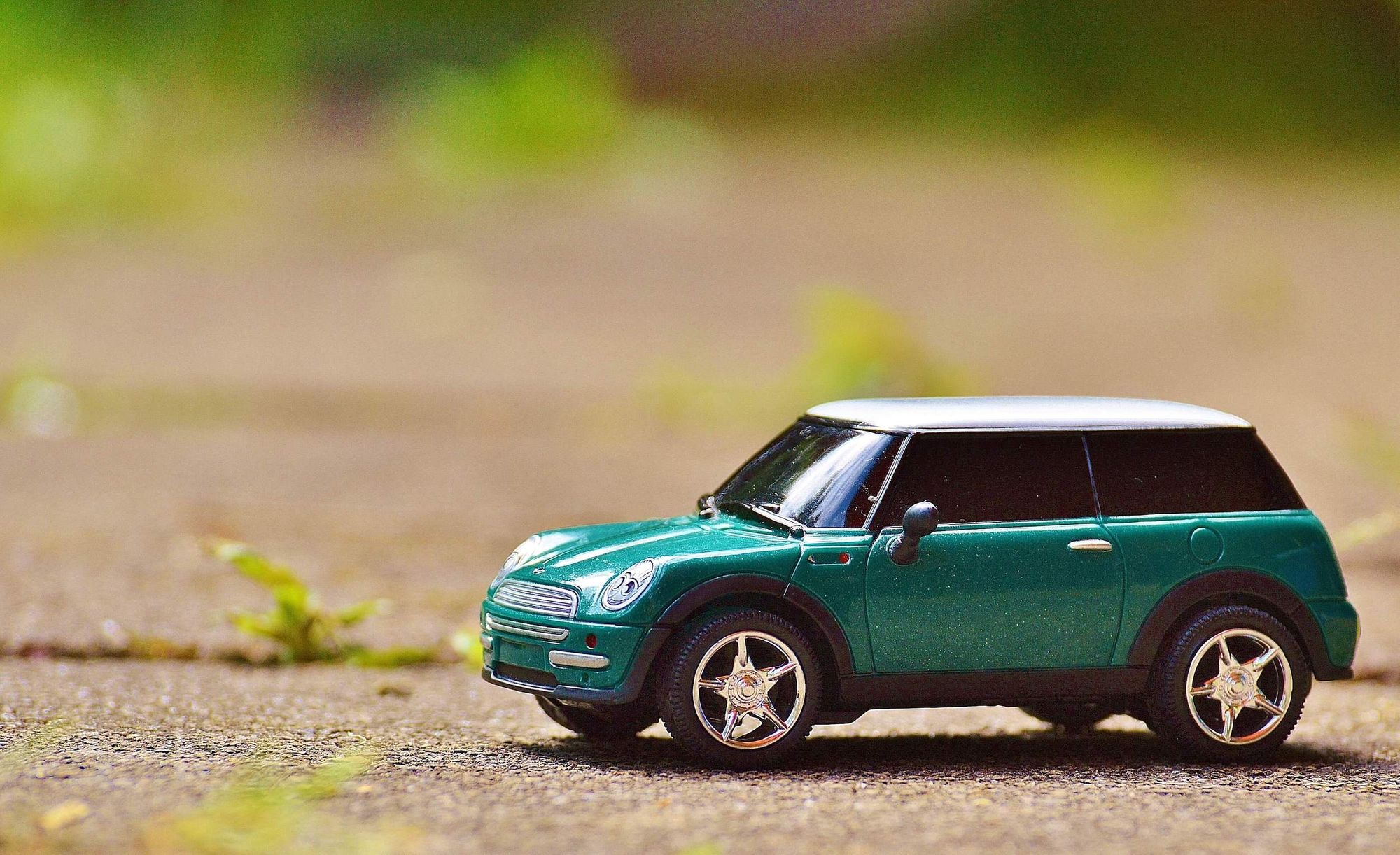 miniature car on concrete with plants showing between the gaps