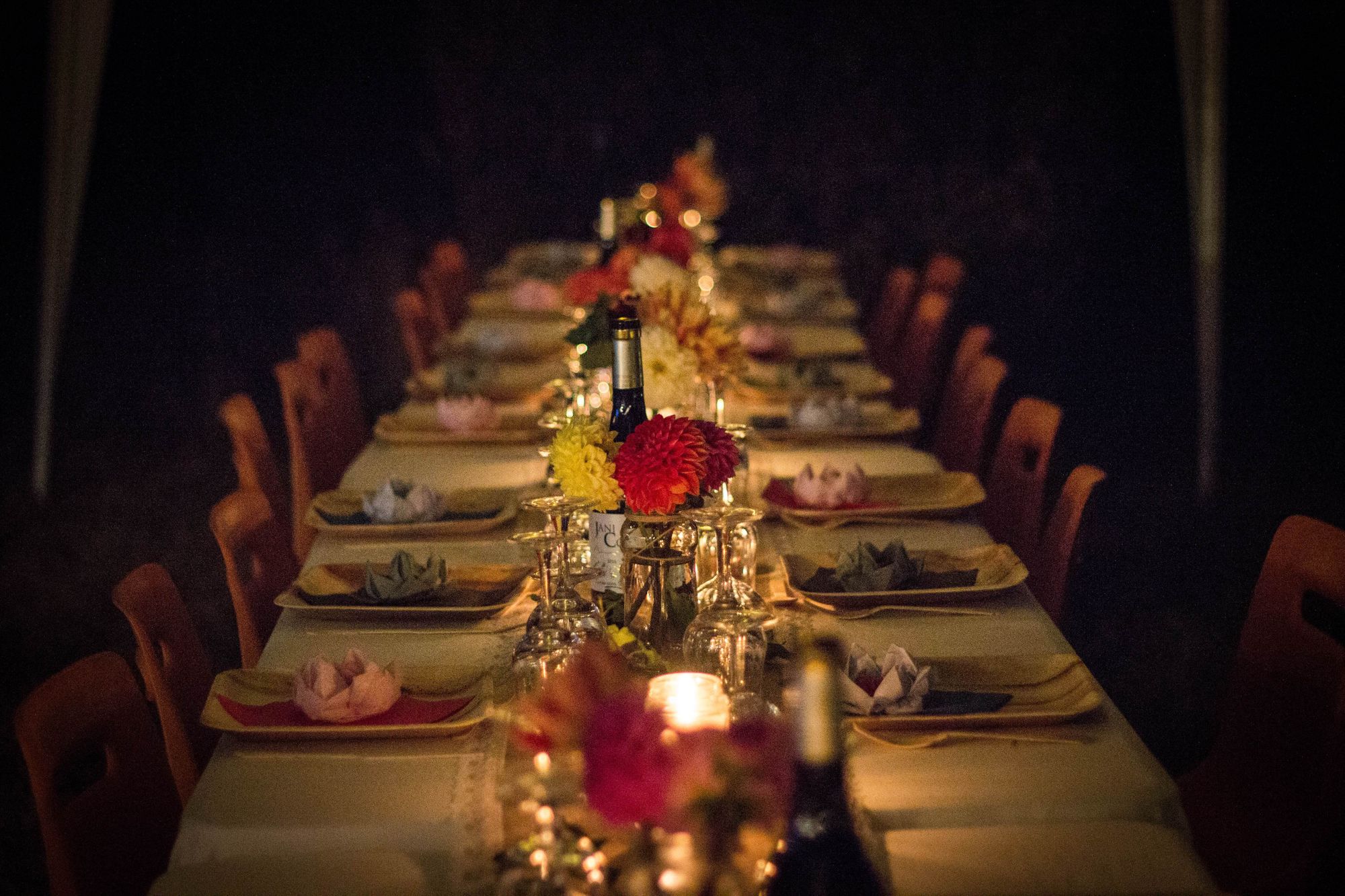 Long table set for a candlelit supper with wine, plates, glasses and flowers