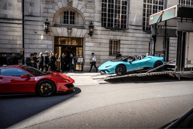 Entrance of Hotel Gotham with red and blue supercars outside 