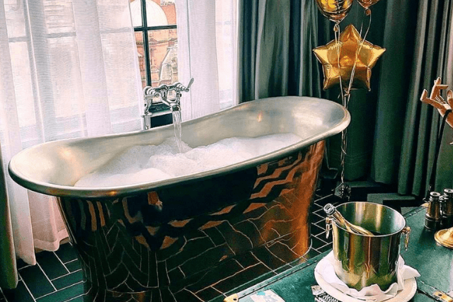 Free-standing gold bath filled with bubbles beside an ice bucket