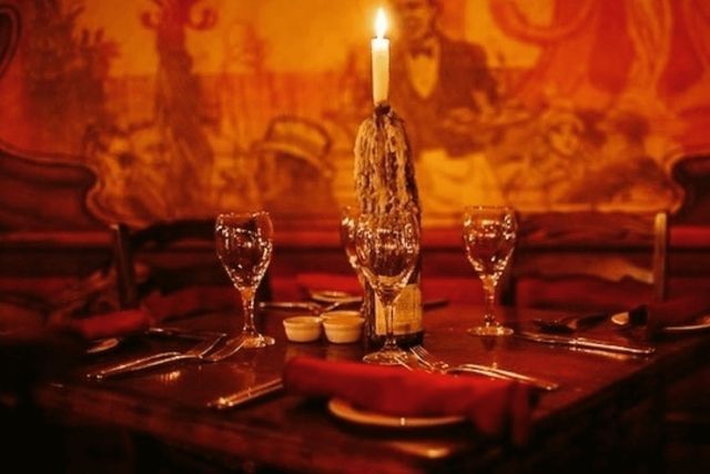 A table set for dinner with glasses and cutlery, and a candle in a wine bottle with dripped wax