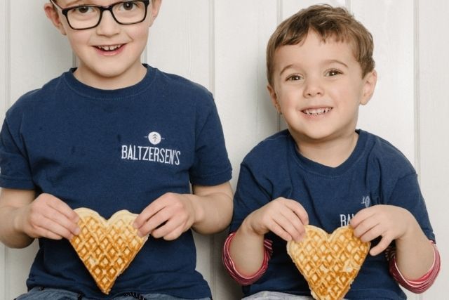 Two young boys holding up heart-shaped waffles, wearing Baltzersen's branded t-shirts