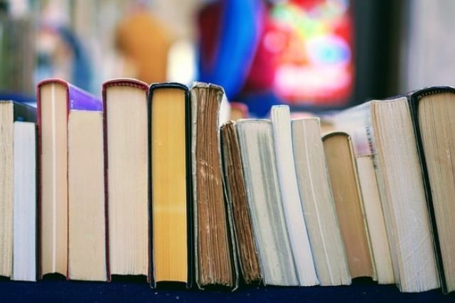 Hardback and paperback books stacked side by side, against a colourful background