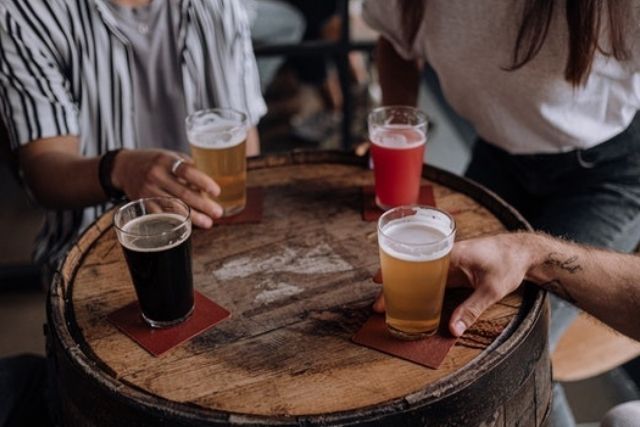 Pints of beer and other drinks on a table made from a beer barrel and people's hands