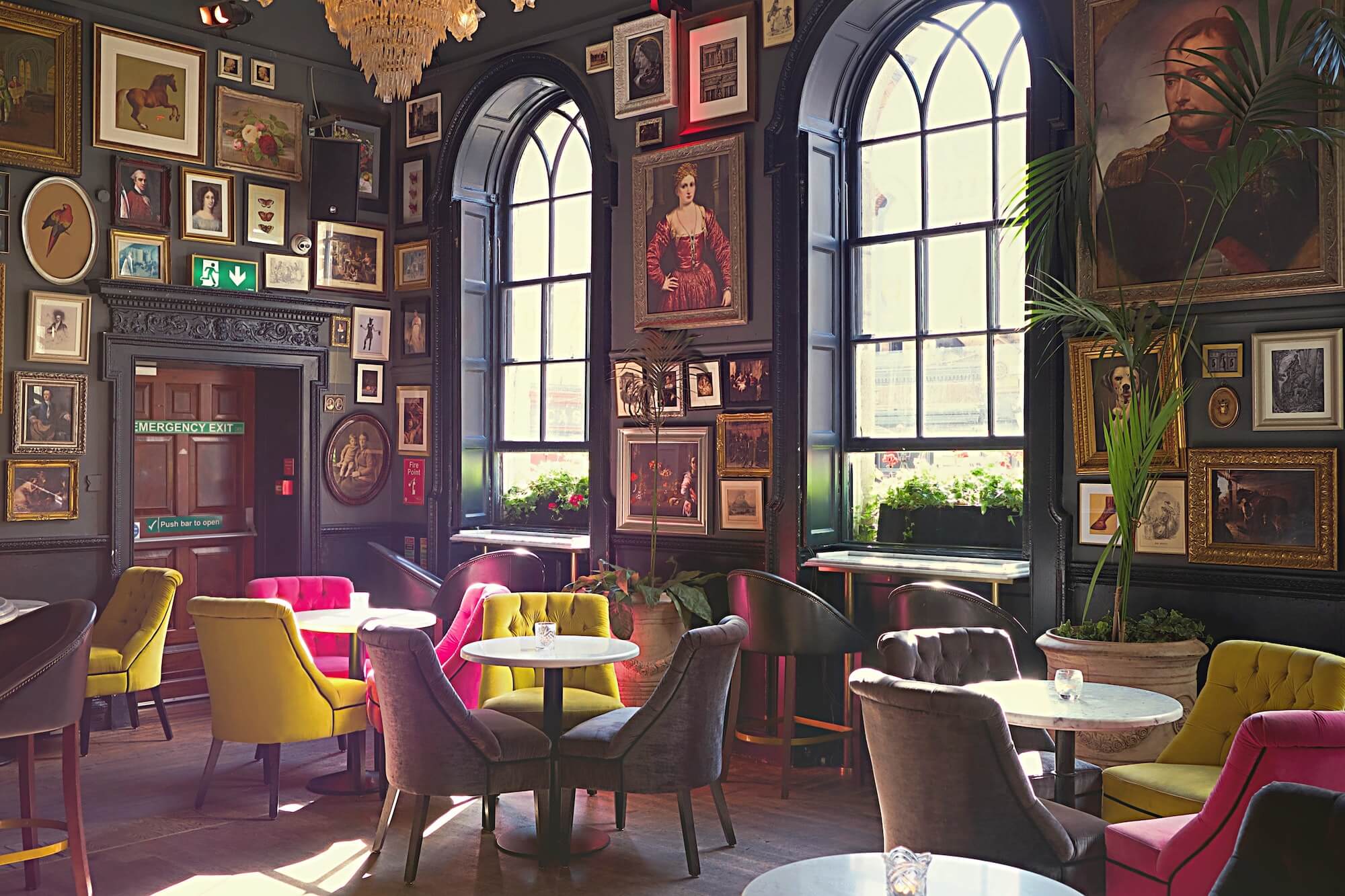 Brightly coloured chairs in a hotel lounge with portraits hanging on grey walls.