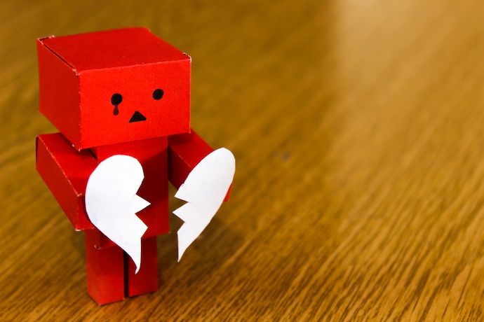 Little red paper robot holding a torn paper heart