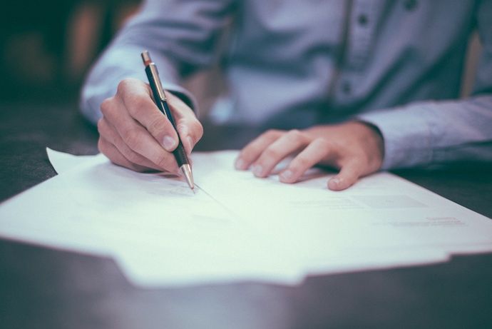 close up photo of man holding a metallic pen above three documents