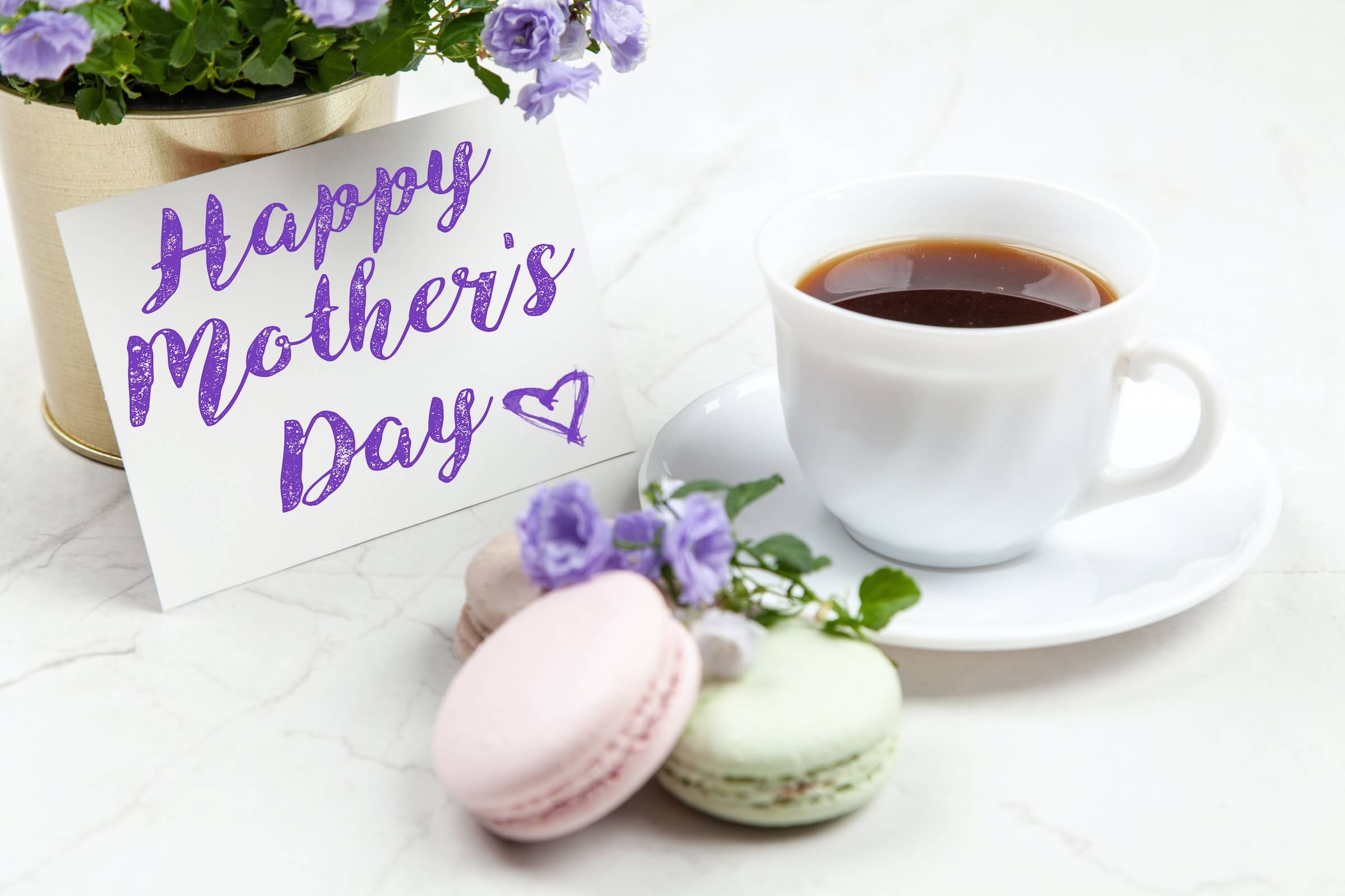 Pink and green macarons with a cup of tea and card reading 'Happy Mother's Day'.