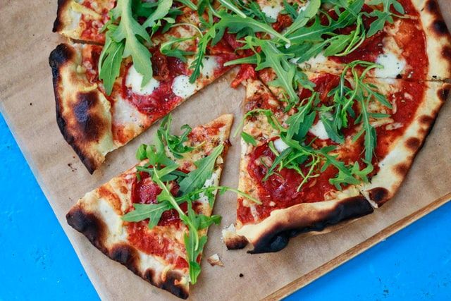 Thin base pizza with tomato, mozzarella and rocket on a wooden board, on a blue table