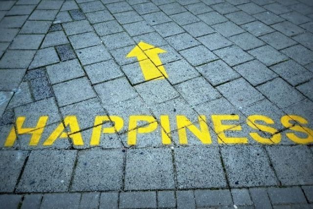 The word 'Happiness' and a directional arrow painted in yellow, on concrete pavement tiles