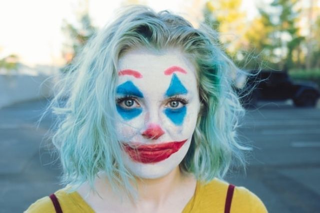 A woman with blue-green hair, and blue and red clown makeup