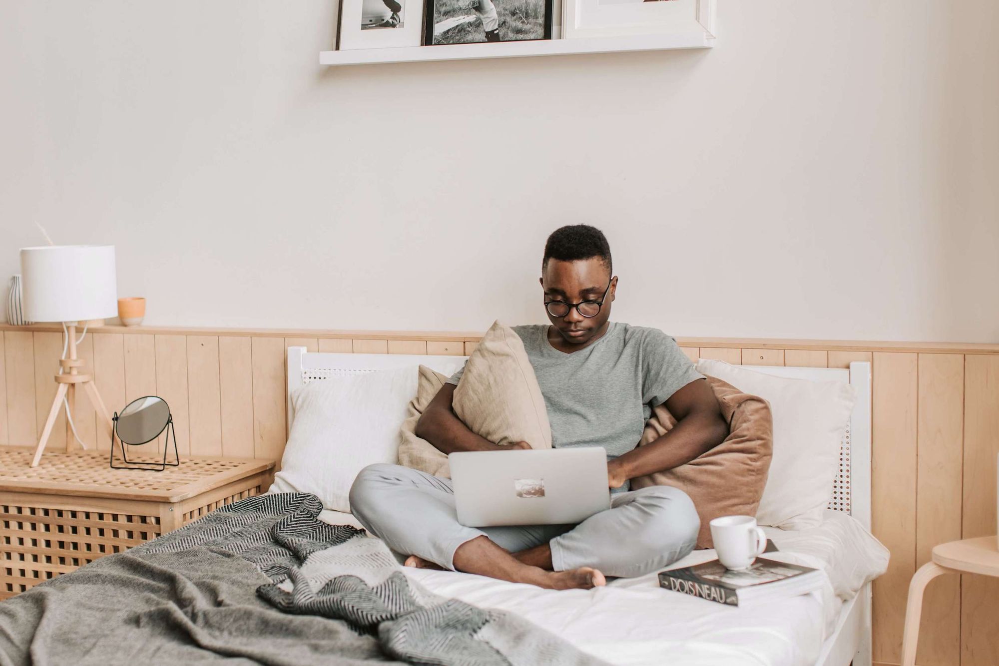 Man sitting on bed in minimalist bedroom using a laptop