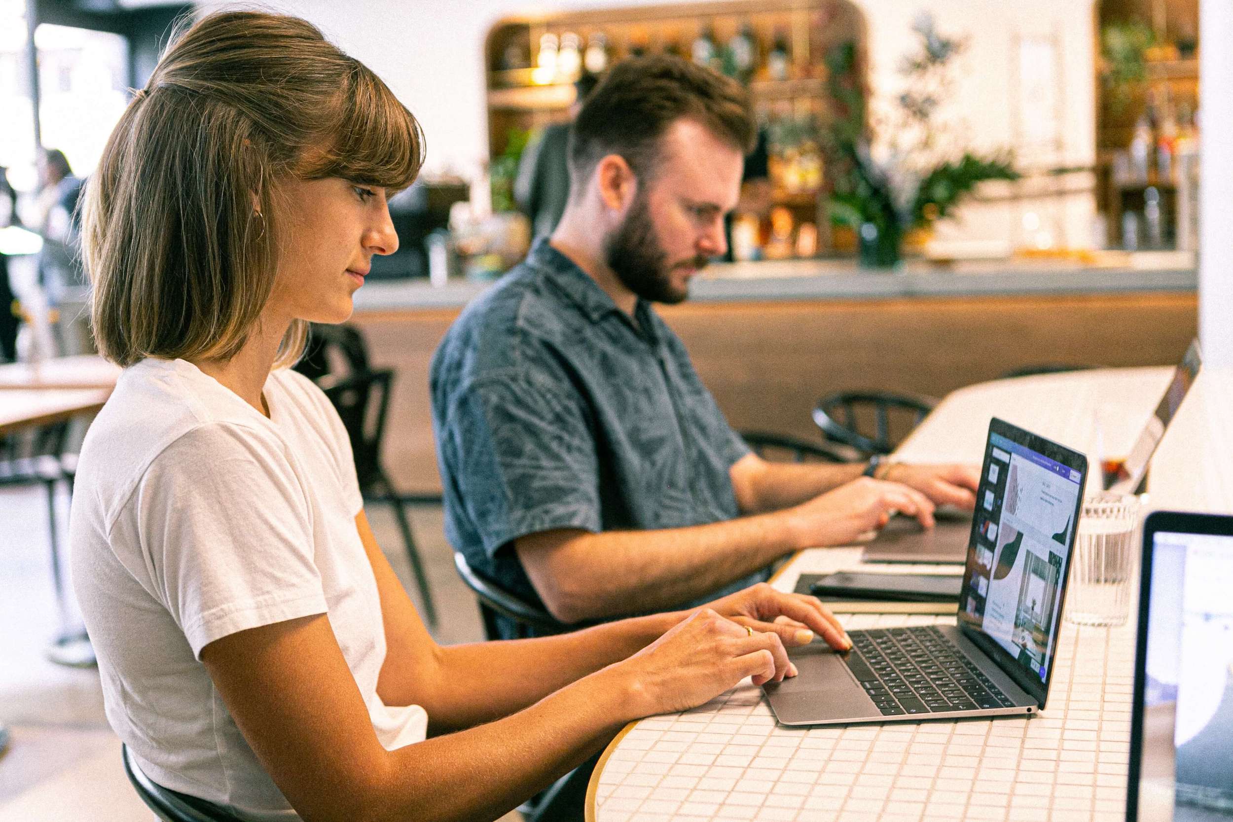 Young woman and bearded man working on laptops at a table.