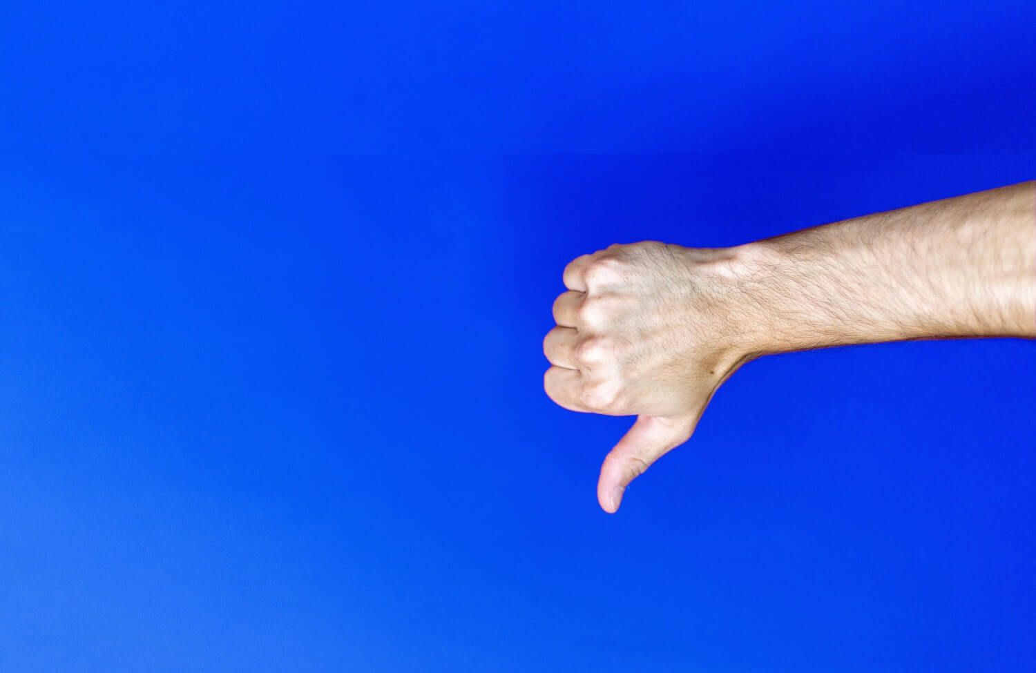Male arm making thumbs down gesture against a dark blue background