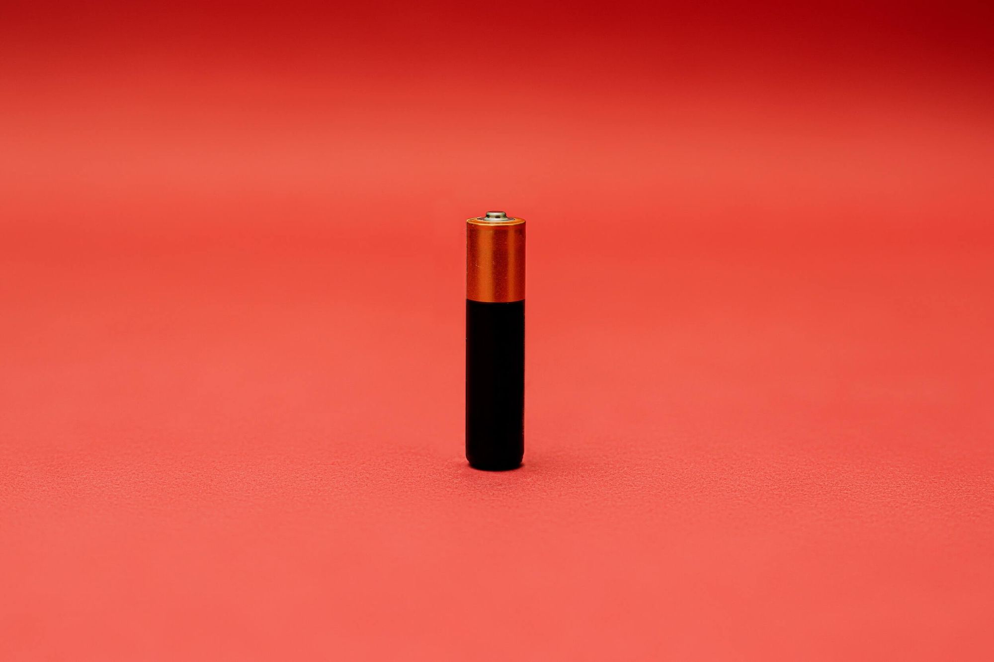 A single Duracell-style battery standing vertically against a pink background. 