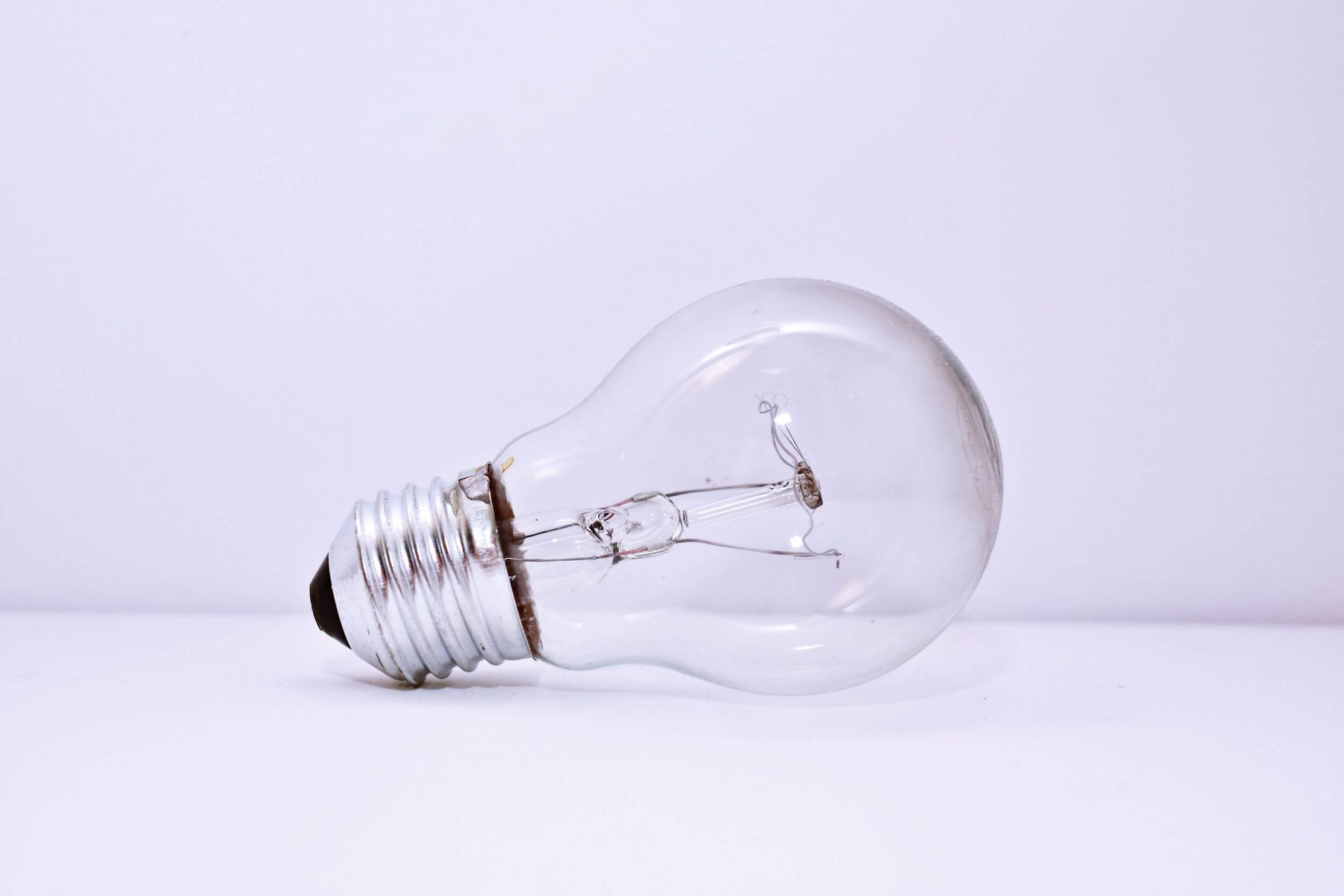 A clear light bulb lying on its side on a white surface with white background