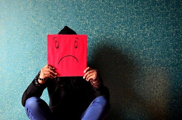 Person holding a sheet of red paper with a sad face drawn on it in front of their face