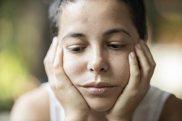 Close up of a woman resting her head in her hands, wearing a pensive expression and looking down.