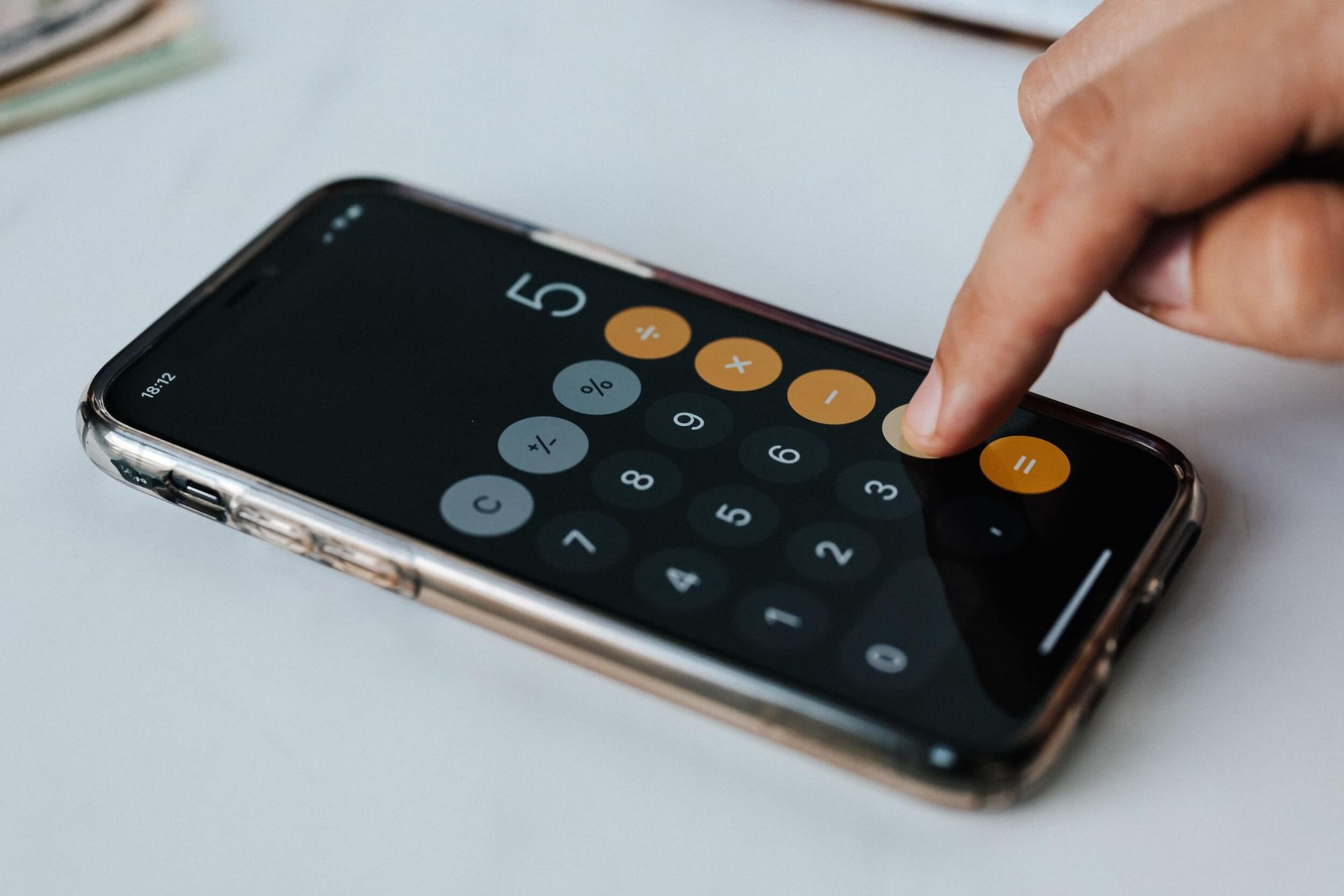 Photo of a smartphone running a calculator app with a hand pressing the plus key.