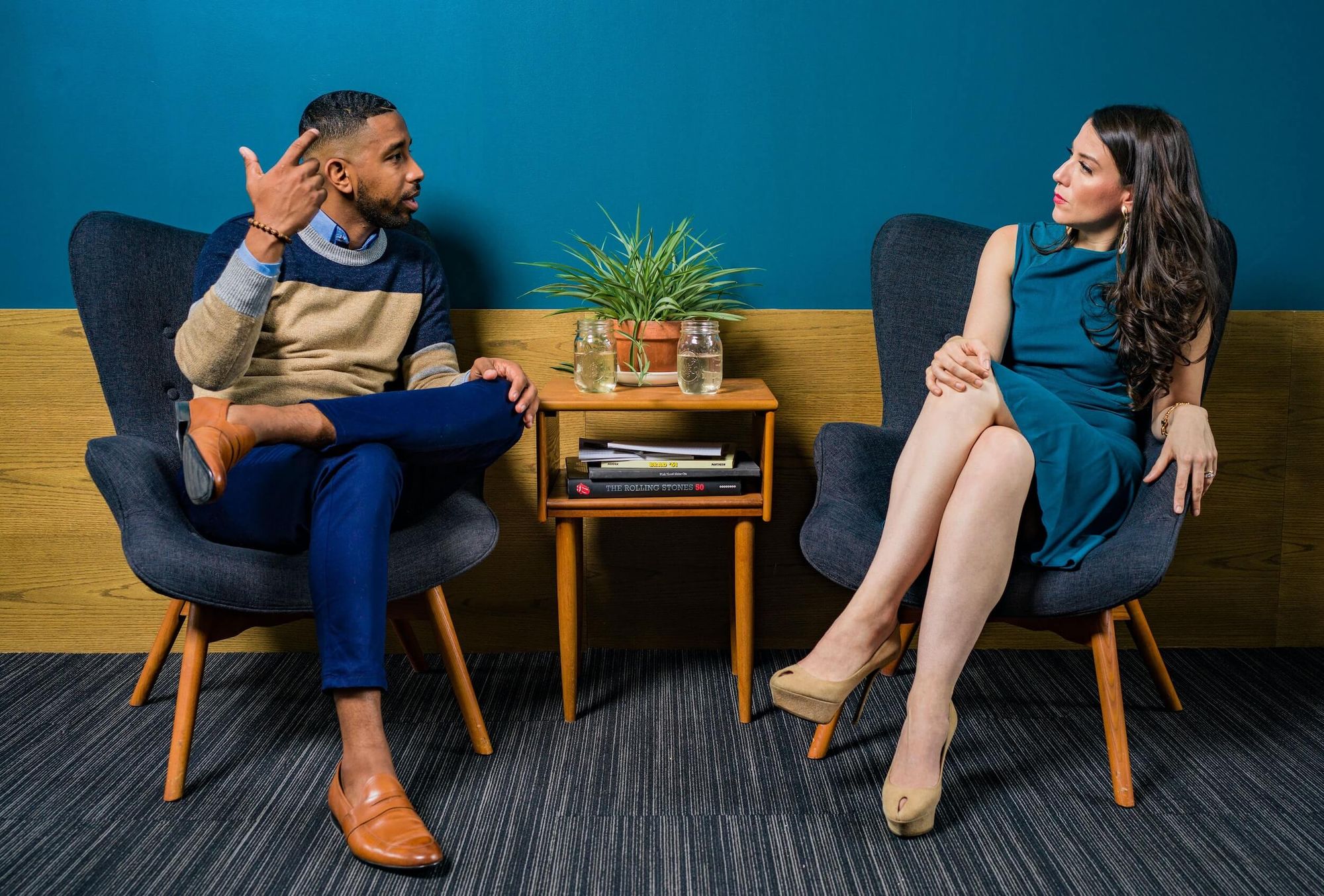 Man and woman in smart attire seated in low armchairs having a conversation.
