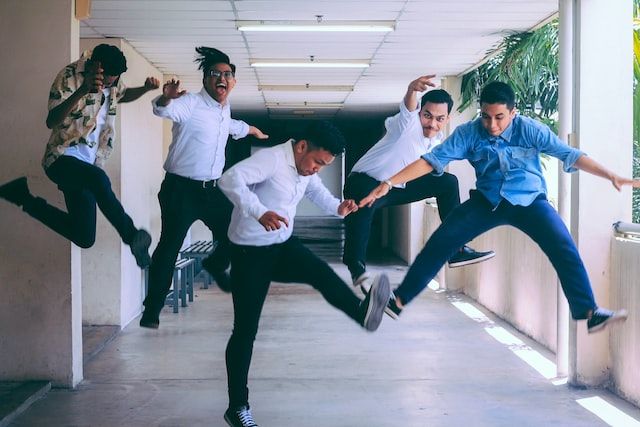Five men in smart casual clothes having fun and jumping into the air, in a sunlit hallway