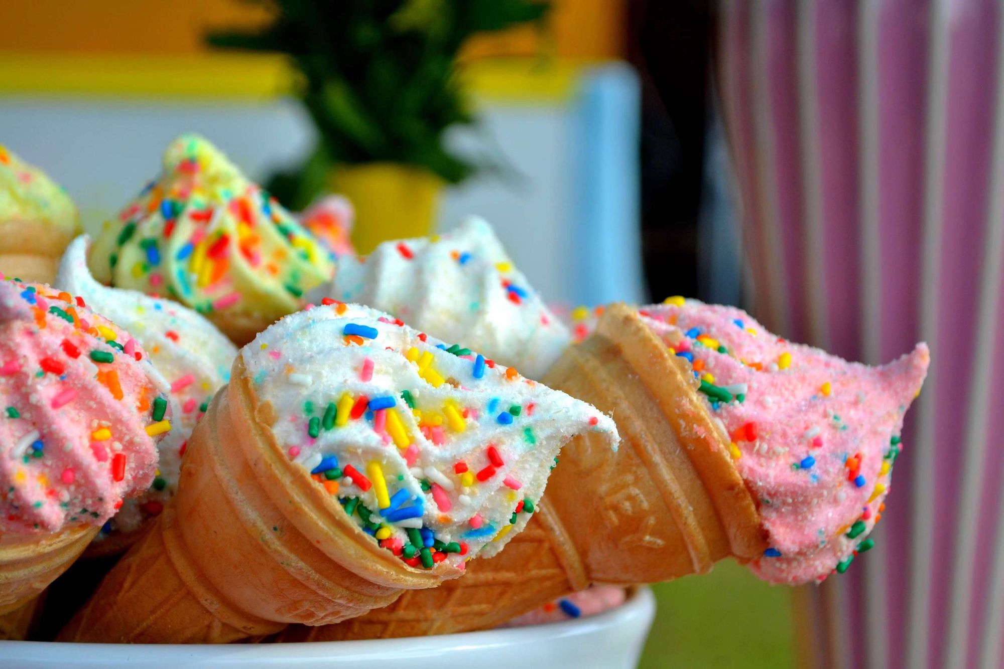 Various brightly coloured ice creams in wafer cones, topped with colourful sprinkles.