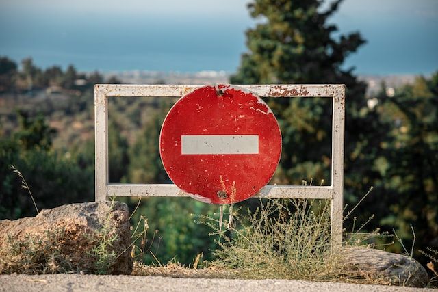 Red "no entry" sign on wooden barrier overlooking a view of the sea