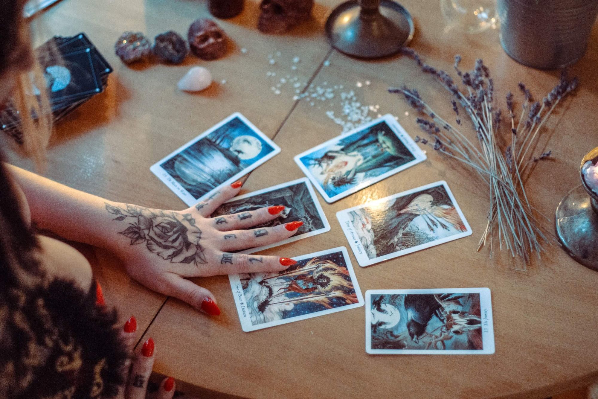Woman with tattooed hands and red fingernails using tarot cards.