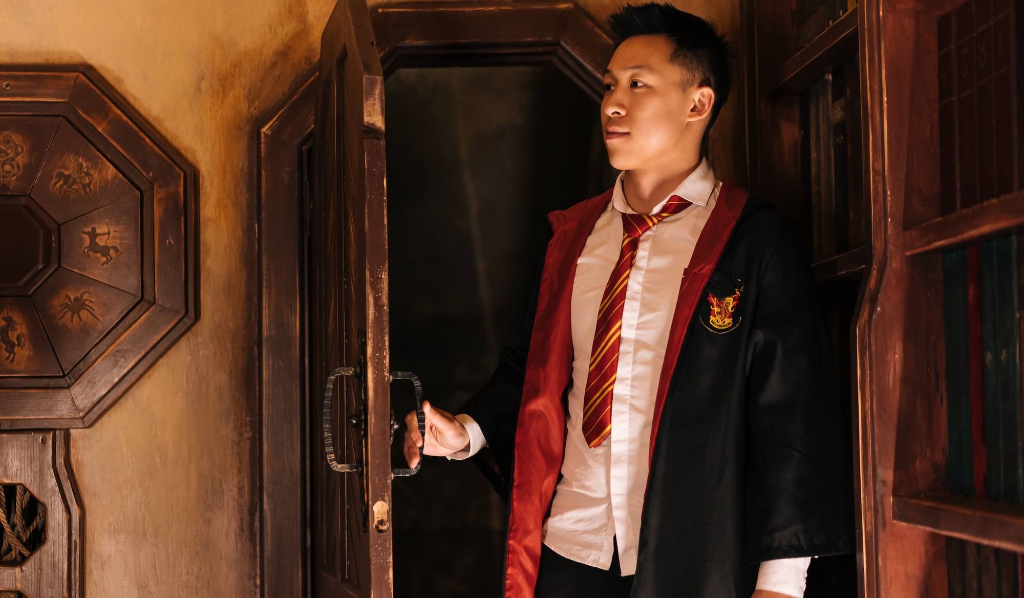 Man wearing Harry Potter style robes and maroon school tie in an old office.