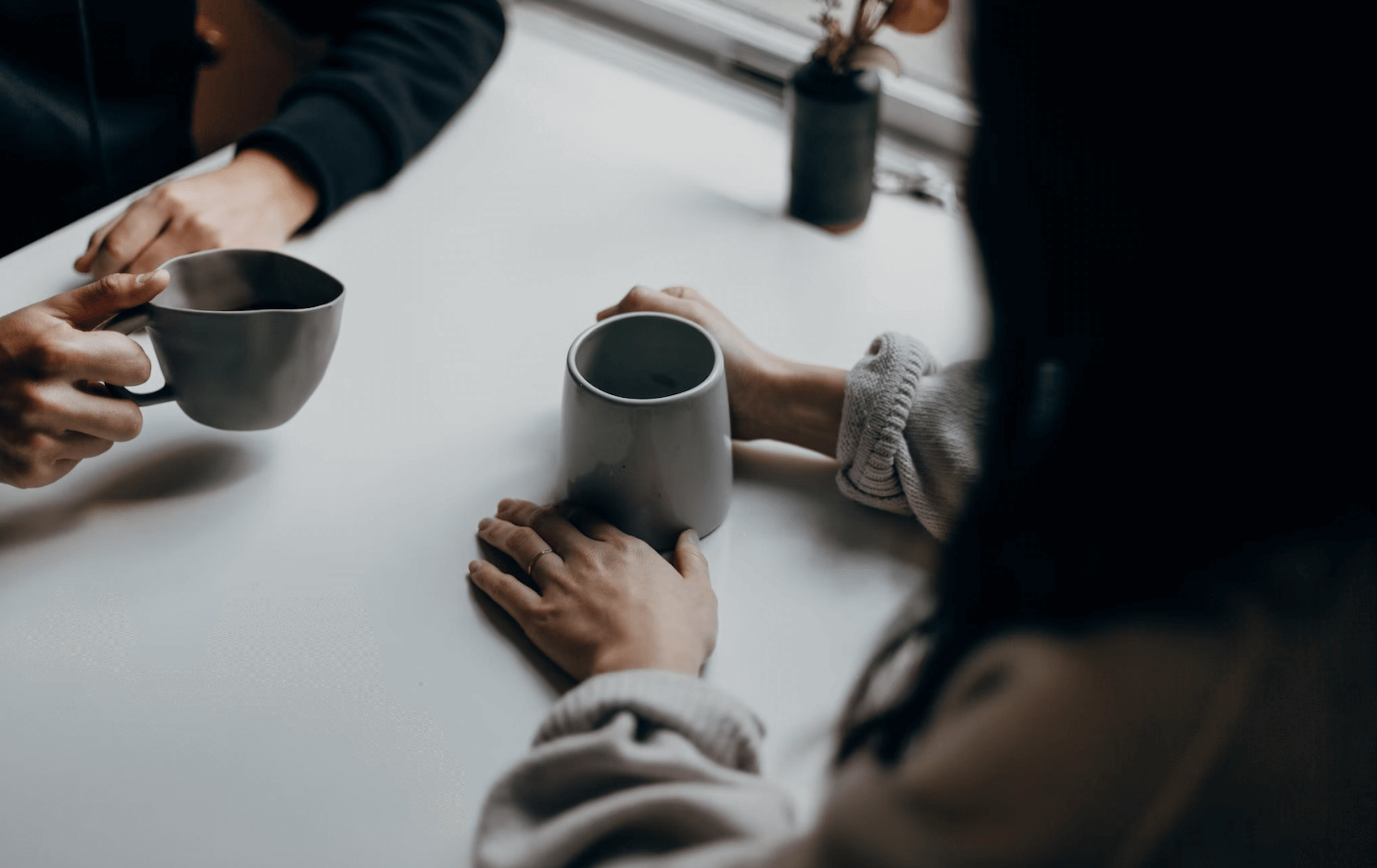 Hands and coffee cups on a table as two people engage in conversation.