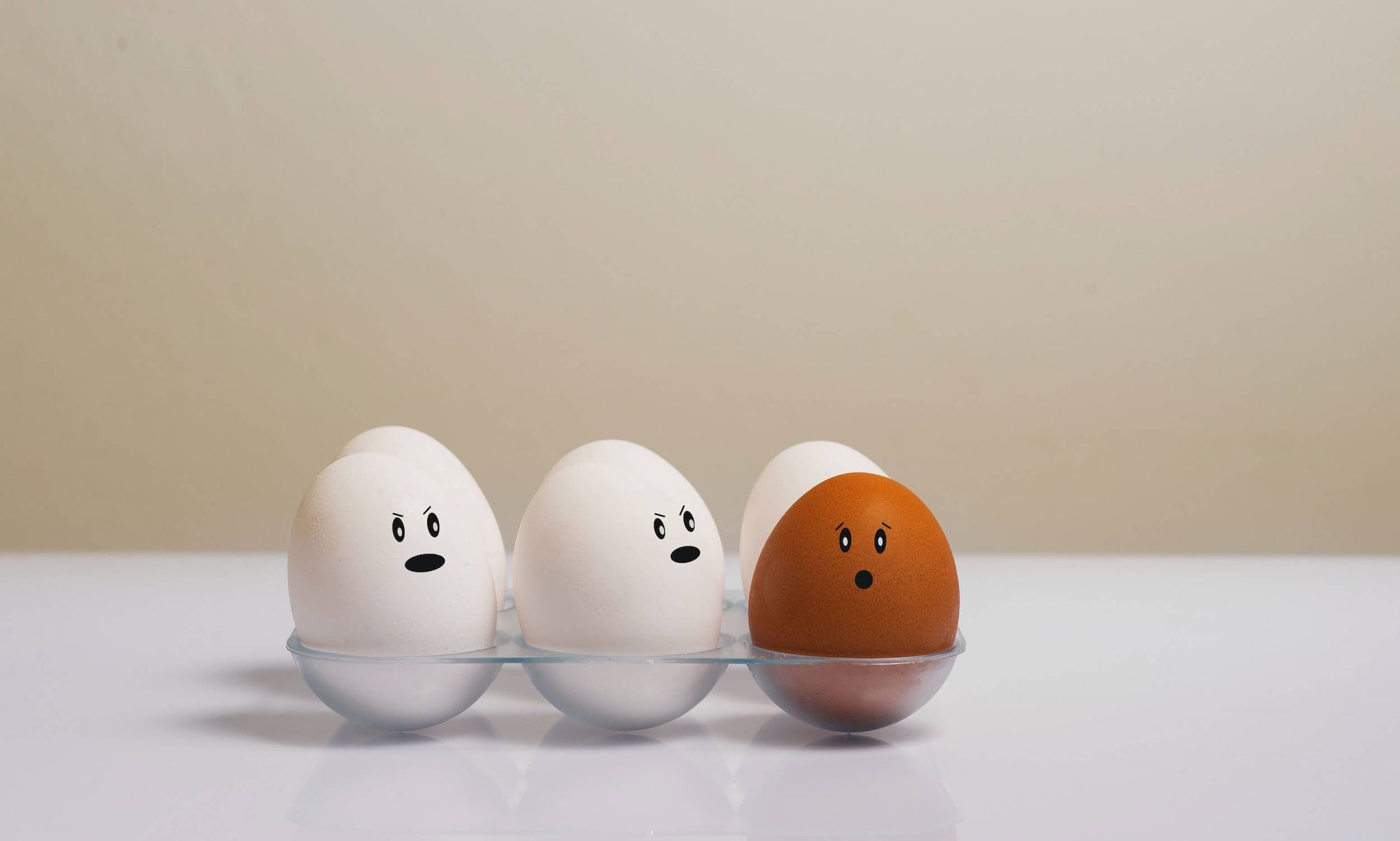 White eggs in an egg holder with one brown egg with shocked face drawn on it