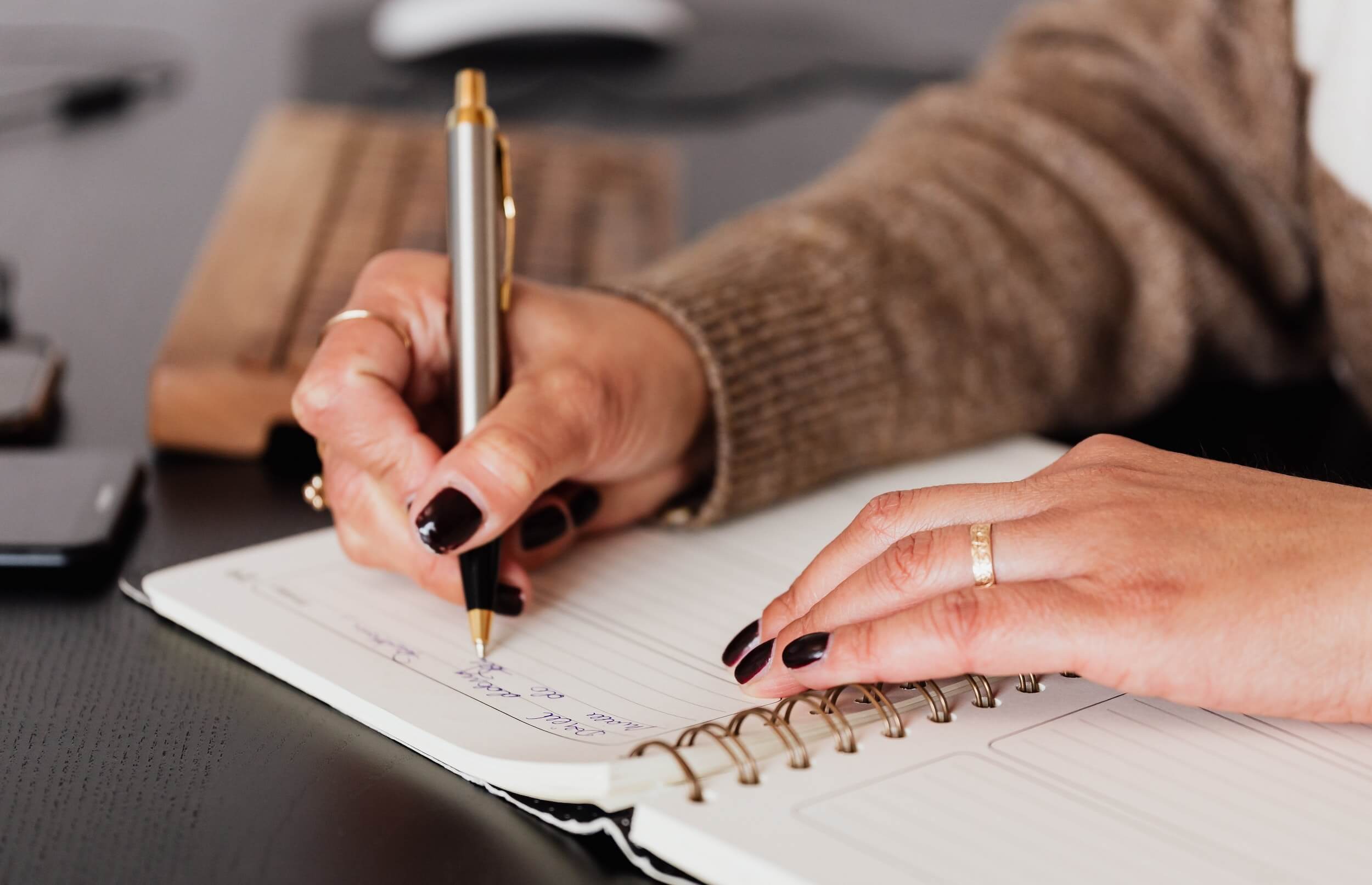 Closeup of a woman with painted nails writing in a notebook.