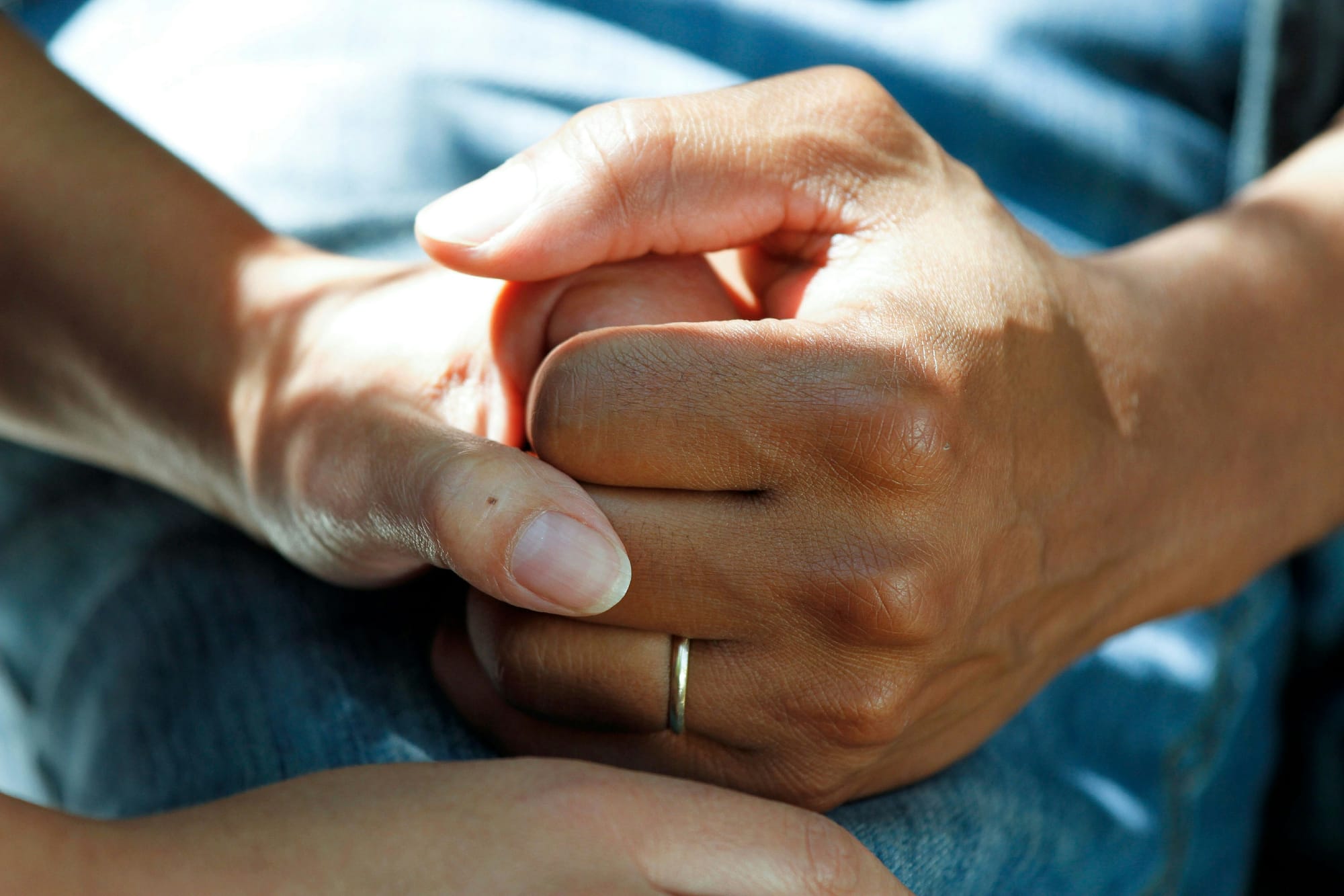 A close up of two people holding hands. One hand has a wedding band on their finger.
