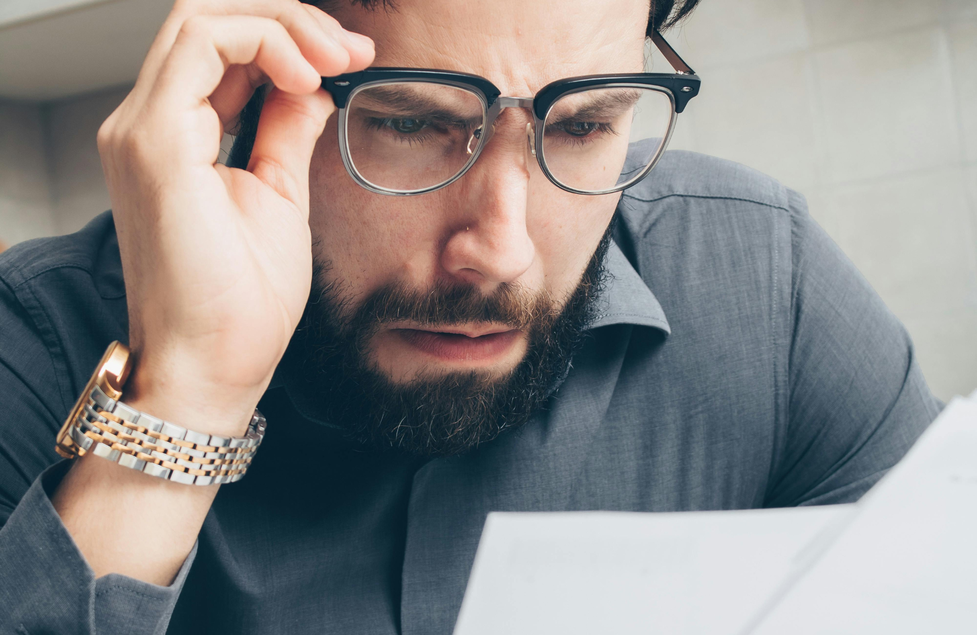 A bearded comically peering through his glasses in confusion at a report.