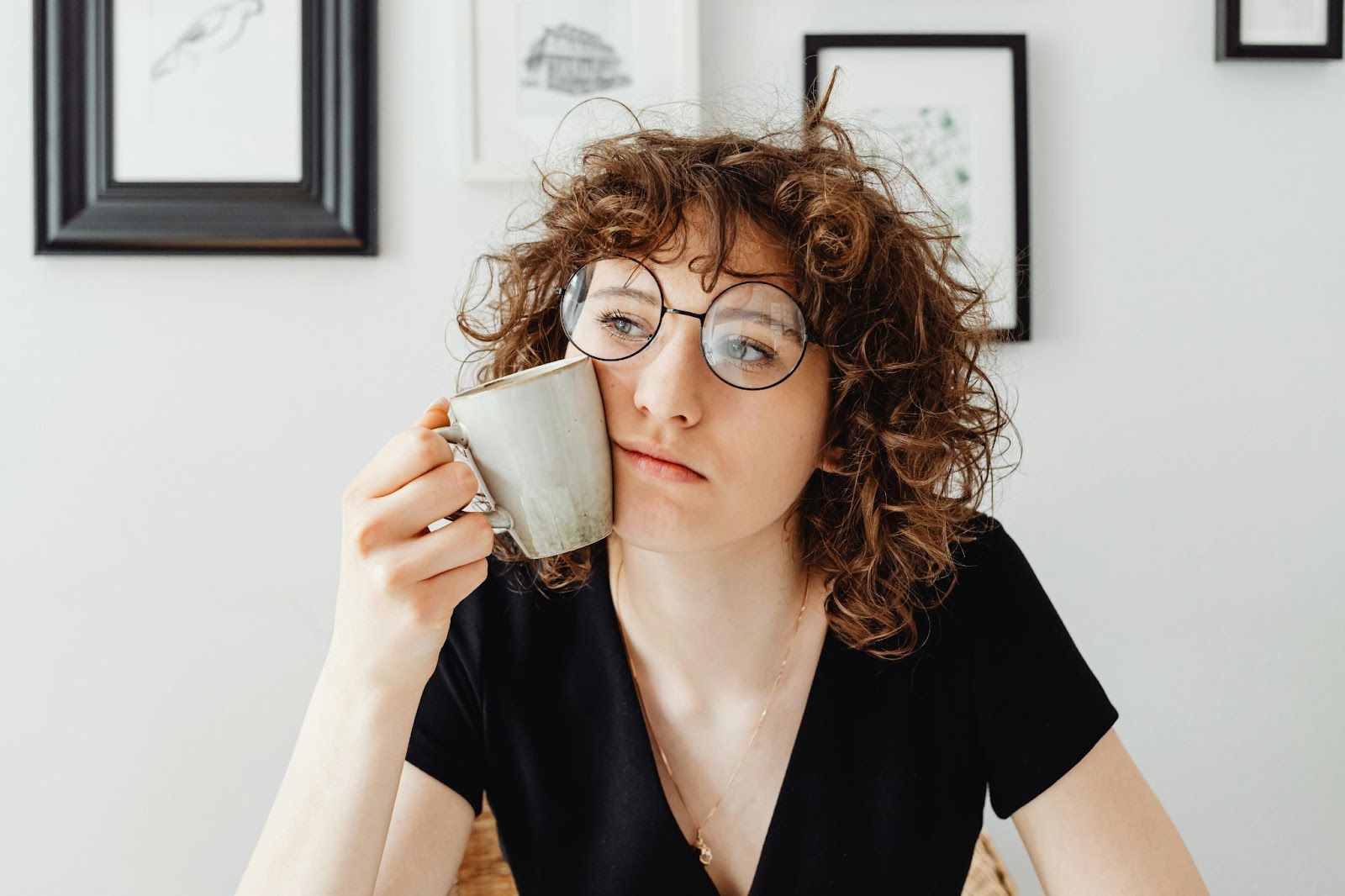 A woman holding a mug to her cheek and leaning into it, bored.