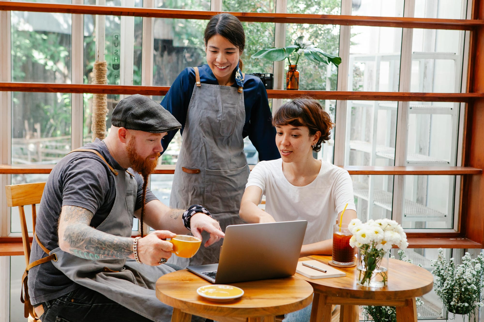 Three hospitality workers sat in a cafe, relaxed and smiling as they look at a laptop screen.