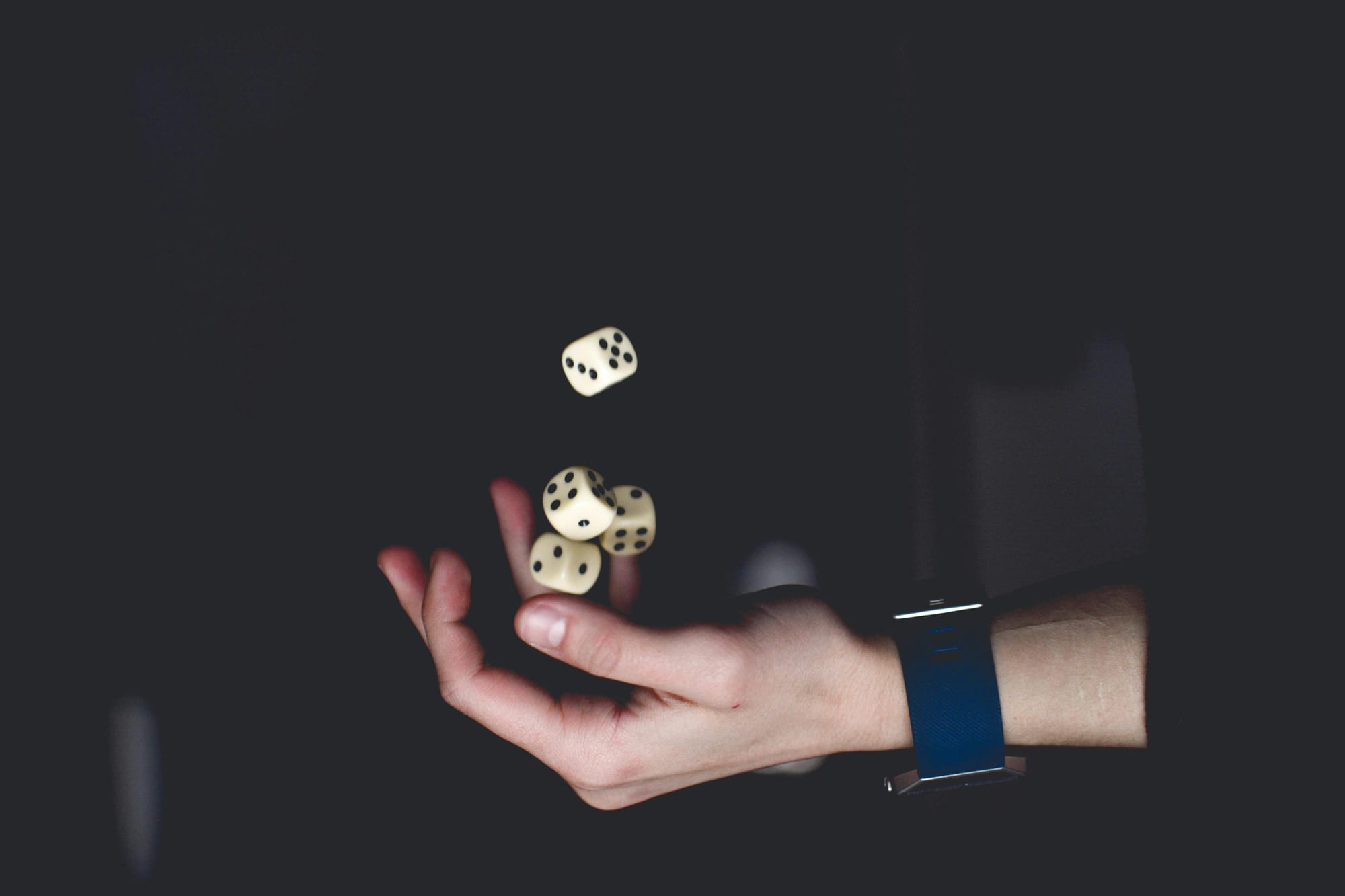 A hand in darkness, throwing dice in the air.
