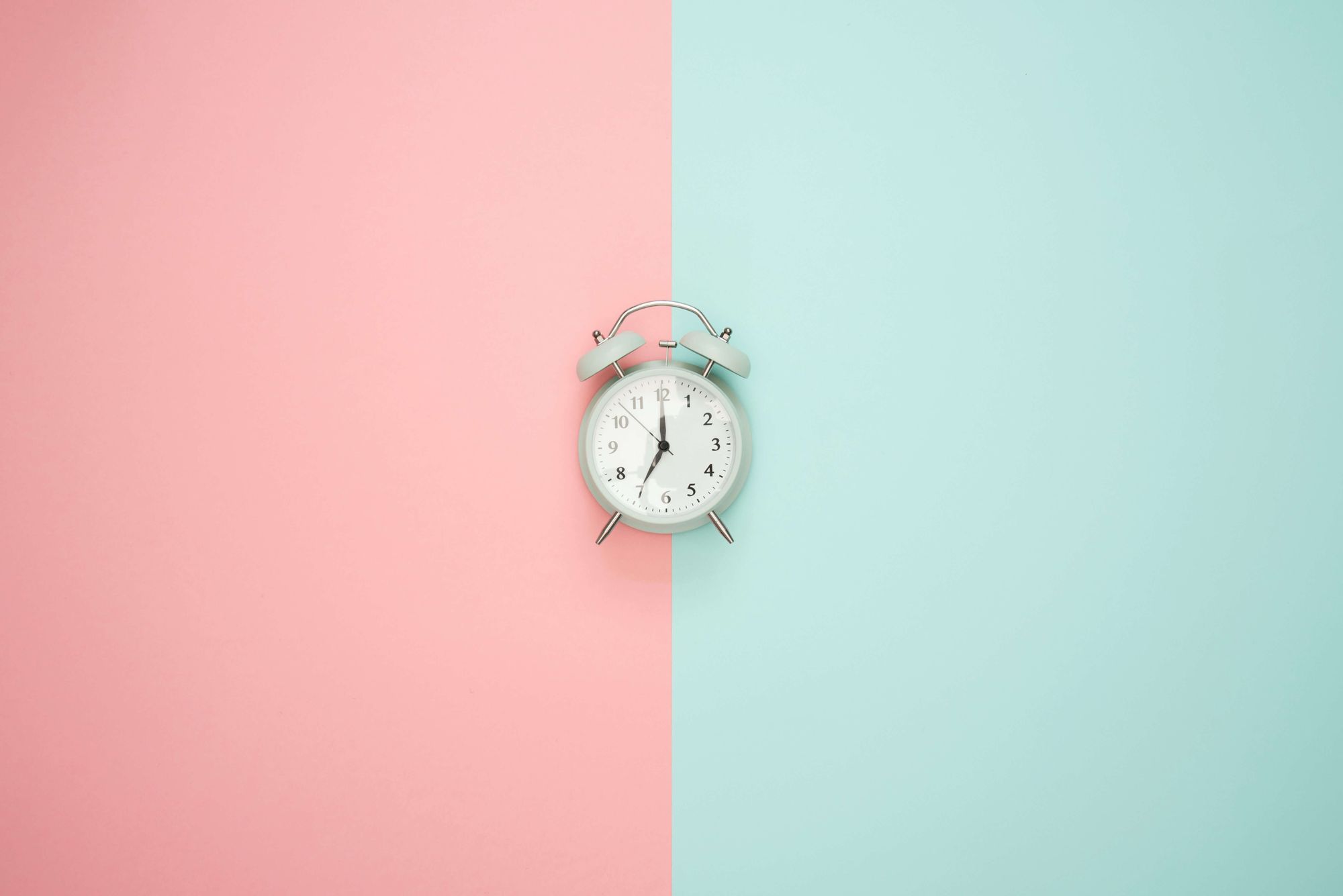 An old-fashioned alarm clock in front of a pastel pink and green background