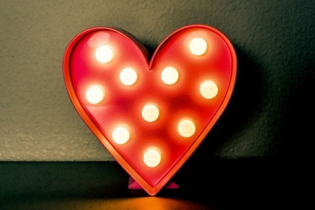 A red heart-shaped light box, leaning against a dark wall.