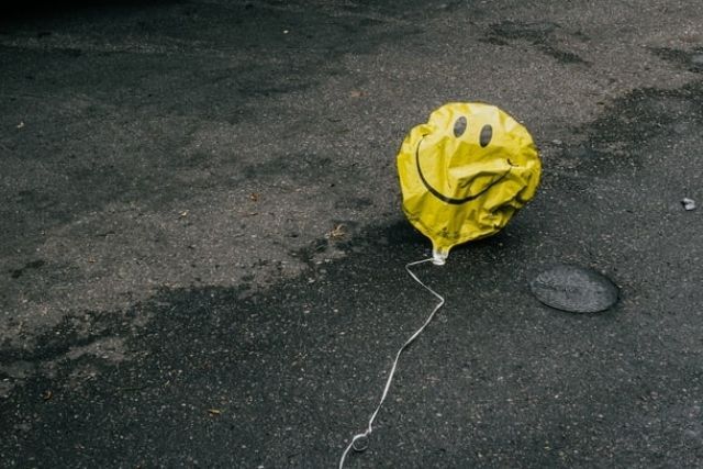 Deflated smiley face balloon, lying on the concrete