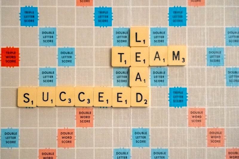 A Scrabble game board with the words 'lead', 'team' and 'succeed' spelled out in beige Scrabble tiles.