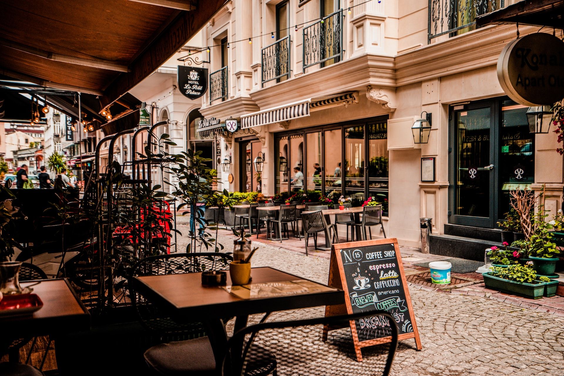 Cafe-lined cobbled street in a city centre, with awnings, outdoor tables and chairs, and a blackboard menu