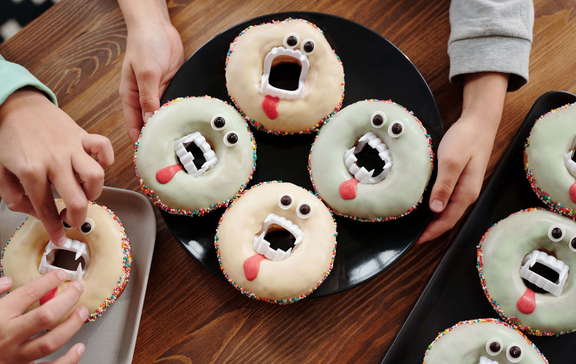 Close up of plates of Halloween-themed doughnuts with false vampire teeth being prepared by children's hands.