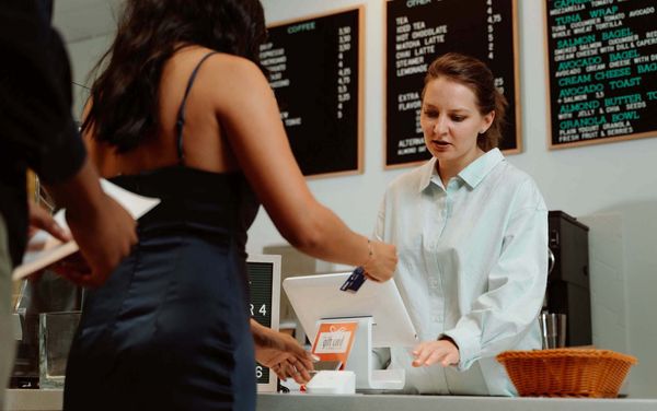 A woman in a dark blue dress paying in a cafe using her credit card.